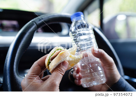Asian woman driver hold ice coffee cup and sandwich bread for eat and drink in car, dangerous and risk an accident. 97354072