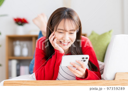 リビングでスマホを見る若い女性　 97359289