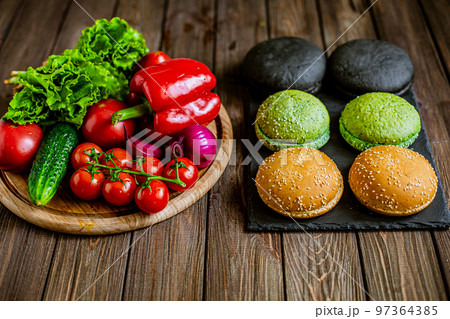 High angle view of variety of six hamburger buns with vegetables on the table. Black, green, yellow High angle view of variety of six hamburger buns with vegetables on the table. Black, green, yellow 97364385