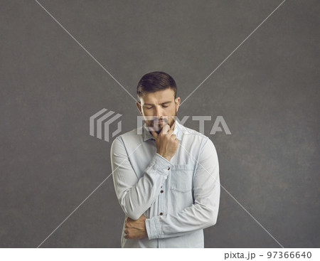 Serious puzzled sad man thinking looking down keeping fist at chin studio shot 97366640