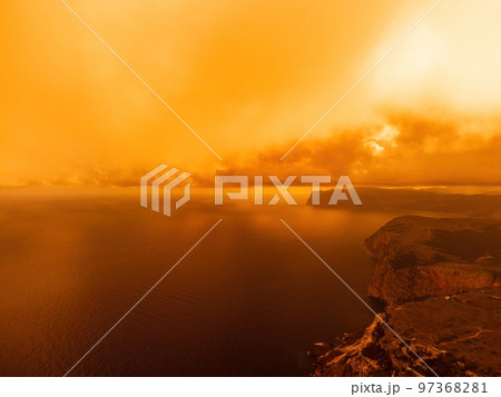 Aerial view red burning sunset over the sea with rocky volcanic cliff. Abstract nature summer sunset ocean sea background. Small waves on golden warm water surface Evening. Horizon. Nobody. No people. 97368281