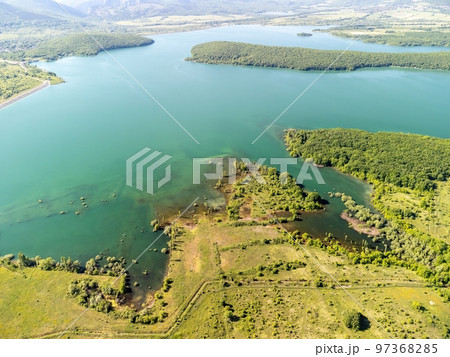 Aerial view on mountain lake. Drone over water reservoir at mountain valley covered with green spring forest. Beautiful view from above on smooth blue surface of mountain lake among highlands. Nobody Aerial view on mountain lake. Drone over water reservoir at mountain valley covered with green spring forest. Beautiful view from above on smooth blue surface of mountain lake among highlands. Nobody 97368285