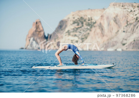 Woman sup yoga. Middle age sporty woman practising yoga pilates on paddle sup surfboard. Female stretching doing workout on sea water. Modern individual female hipster outdoor summer sport activity. Woman sup yoga. Middle age sporty woman practising yoga pilates on paddle sup surfboard. Female stretching doing workout on sea water. Modern individual female hipster outdoor summer sport activity. 97368286
