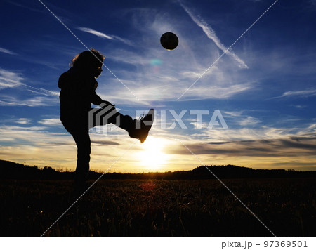 Boy kicking the ball on an empty field at sunset 97369501