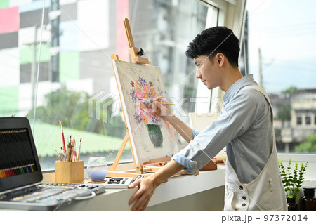 Concentrated man painting picture on canvas near window at art workshop. Leisure activity, creative hobby and art concept 97372014