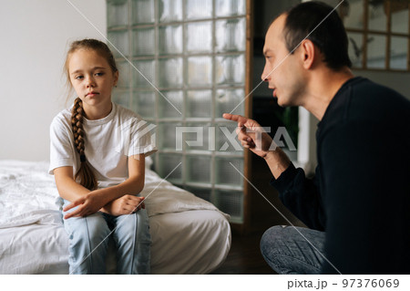 Portrait of loving young father having serious conversation with naughty adorable little daughter , talking about rules to her sitting on bed at home. Concept of dad-daughter problem in preteen years. Portrait of loving young father having serious conversation with naughty adorable little daughter , talking about rules to her sitting on bed at home. Concept of dad-daughter problem in preteen years. 97376069