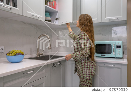 Cute young housewife opens the kitchen cabinet door 97379530