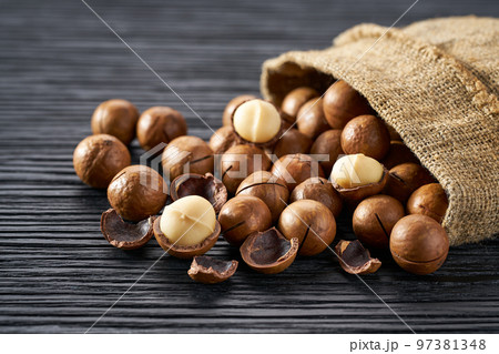 Macadamia are poured out of the bag on a black table, close-up. Macadamia are poured out of the bag on a black table, close-up. 97381348