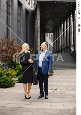Confident businesspersons talking in front of modern office building. Man and woman have business conversation. Banking and financial market concept. Confident businesspersons talking in front of modern office building. Man and woman have business conversation. Banking and financial market concept. 97384772