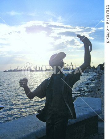Monument to fisherman and fish against backdrop of sunset in Berdyansk 97387811