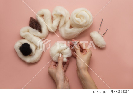 woman hand holding needle felting kit. felted woolen needle and skein of wool on pink table, flat lay woman hand holding needle felting kit. felted woolen needle and skein of wool on pink table, flat lay 97389884