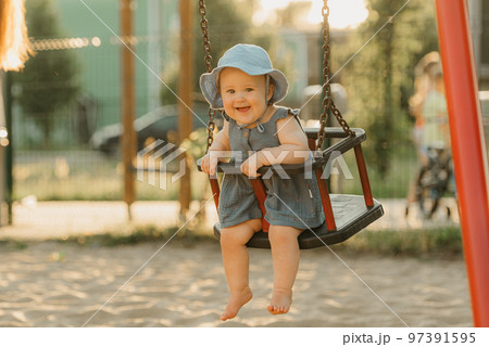 Toddler baby girl in a dress on a swing on the warm summer evening 97391595