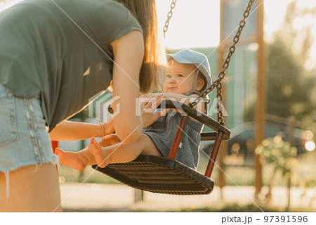 Baby girl in a dress with her mother on a swing on the warm summer evening 97391596