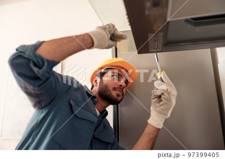 Handyman in uniform repairing kitchen extractor, replacing filter in cooker hood.Maintenance concept 97399405