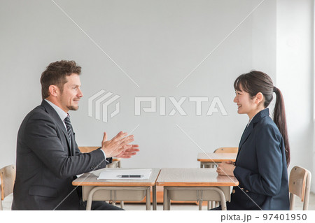 学校で志望校について進路相談・二者面談・面接練習を行う教師と笑顔のアジア人の高校生 97401950