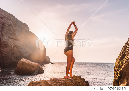 Young woman with long hair in black swimsuit and boho style braclets practicing outdoors on yoga mat by the sea on a sunset. Women's yoga fitness routine. Healthy lifestyle, harmony and meditation Young woman with long hair in black swimsuit and boho style braclets practicing outdoors on yoga mat by the sea on a sunset. Women's yoga fitness routine. Healthy lifestyle, harmony and meditation 97406236
