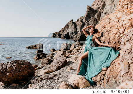 Side view a Young beautiful sensual woman with black hair in a long mint dress posing on a beach with calm sea bokeh lights on sunny day. Girl on the nature on blue sky background. Fashion photo 97406301