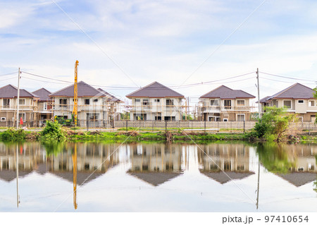 New house building reflection with water in lake at residential estate construction site with clouds and blue sky New house building reflection with water in lake at residential estate construction site with clouds and blue sky 97410654