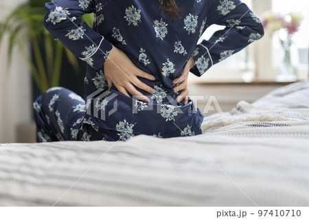腰をおさえるパジャマ姿のアラフィフの女性の後ろ姿 97410710