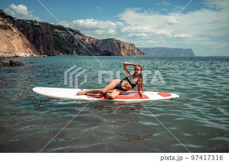 Woman sap sea. Sports girl on a surfboard in the sea on a sunny summer day. In a black bathing suit, he sits on a sapa in the sea. Rest on the sea. 97417316