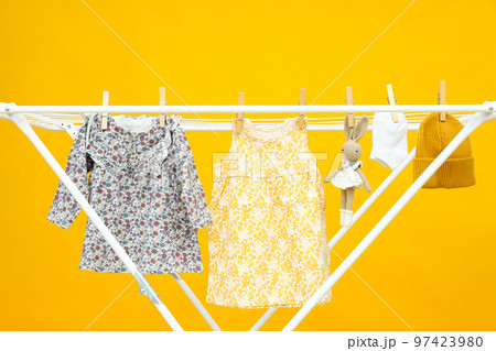 Child clothes and toy hanging and drying on drying rack on yellow background Child clothes and toy hanging and drying on drying rack on yellow background 97423980