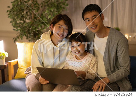 夜　ソファに並んでノートパソコンを見る小学生の女の子とパパとママ 97425924