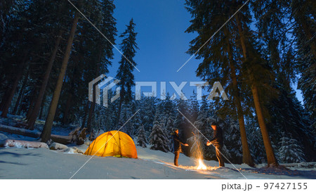 couple camping with campfire and tent outdoors in winter forest 97427155