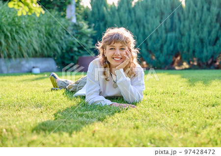 Portrait of cute teenage girl lying on grass looking at camera Portrait of cute teenage girl lying on grass looking at camera 97428472