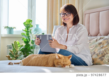 Middle aged woman at home on couch with laptop and cat 97428677