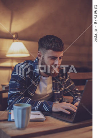 Young professional surfing the Internet on his laptop in a cafe Young professional surfing the Internet on his laptop in a cafe 97429681