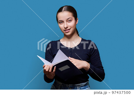 Teenager female student with notebook looking at camera on blue background 97437500