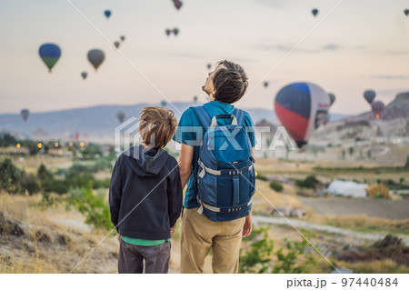 Tourists father and son looking at hot air balloons in Cappadocia, Turkey. Happy Travel in Turkey concept. father and son on a mountain top enjoying wonderful view 97440484