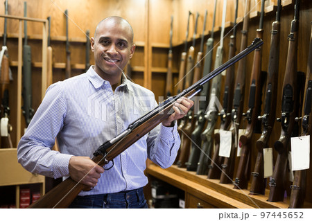 Happy hispanic man standing with hunting rifle at gun shop Happy hispanic man standing with hunting rifle at gun shop 97445652