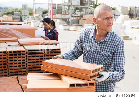 Worker stacking bricks in warehouse of materials Worker stacking bricks in warehouse of materials 97445894