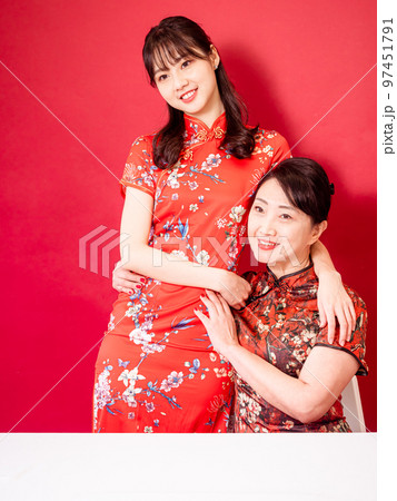 伝統的なチャイナ ドレスを着て、赤い背景に寄り添って微笑む娘と母の肖像画。 伝統的なチャイナ ドレスを着て、赤い背景に寄り添って微笑む娘と母の肖像画。 97451791
