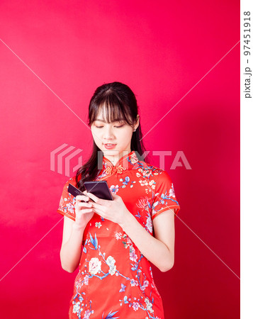 赤い背景にスマートフォンを使って、伝統的なチャイナドレスを着たアジアの若い女性のポートレート。 97451918