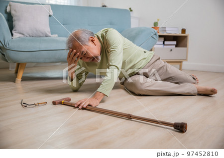 Sick senior old man falling down lying on floor because stumbled at home alone with wooden cane walking stick in living room, elderly man retired grandfather having accident after standing from sofa 97452810