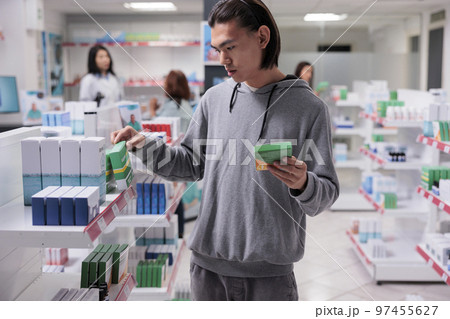 Male asian customer examining supplements on shelves, client looking at pills boxes in drugstore filled with health care products like vitamins and drugs. Searching for medical supplies. 97455627