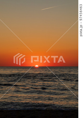 夕暮れの飛行機雲と沈みゆく太陽 97456463