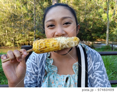 Asian woman eating delicious grilled corn, appetizer, picnic time Asian woman eating delicious grilled corn, appetizer, picnic time 97460409