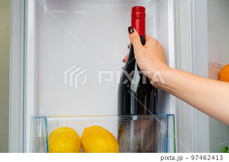 Female hand taking bottle of wine from a fridge 97462413