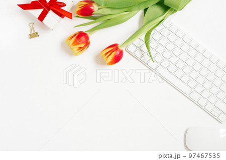 Feminine composition of women's work space, gifts for Mother's Day and Valentine's Day. Gift with a red ribbon and a bouquet of tulip flowers, keyboard. Flat lay and top view 97467535