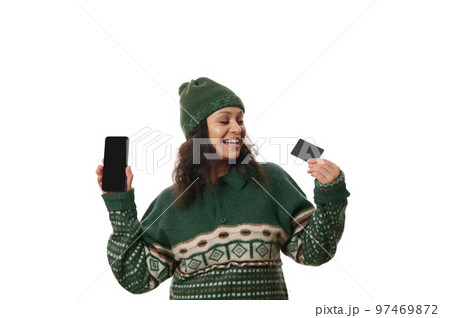 Cheerful Latin American woman, smiling a beautiful toothy smile, showing on camera a black credit card and modern smartphone with space for your advertising text or mobile apps, on white background 97469872