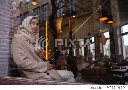 Young muslim woman with smartphone enjoying cup of coffe in cafe. Young muslim woman with smartphone enjoying cup of coffe in cafe. 97471440
