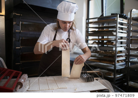 Young baker with chef cap preparing pastries in bakery. 97471809