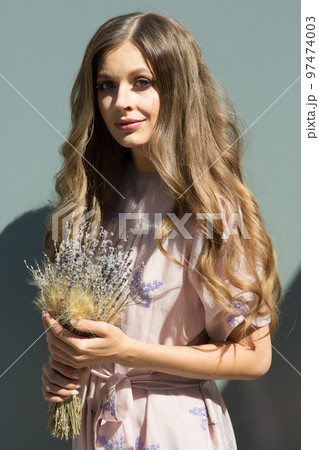 Portrait of a beautiful girl with flowing curly hair, smiling, looking at the camera on the street. Walking around the city, with a bouquet of lavender in your hands. High quality photo 97474003