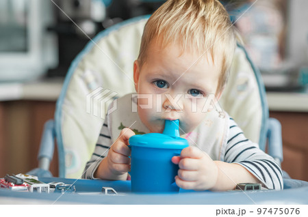 Toddler boy drinks from cup in high chair. Toddler boy drinks from cup in high chair. 97475076