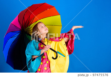 Waterproof accessories for children. Enjoy rainy weather with proper garments. Waterproof accessories make rainy day cheerful and pleasant. Kid girl happy hold colorful umbrella wear waterproof cloak 97475576