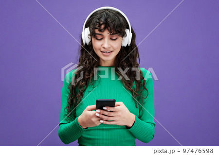 Pretty girl with dark long wavy hair scrolling through playlist in mobile phone 97476598