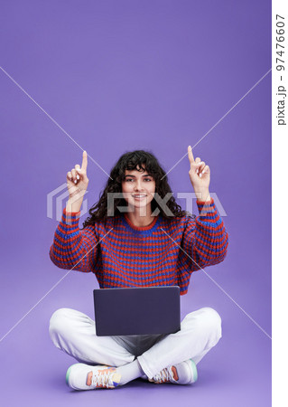 Happy young brunette woman with laptop pointing upwards 97476607